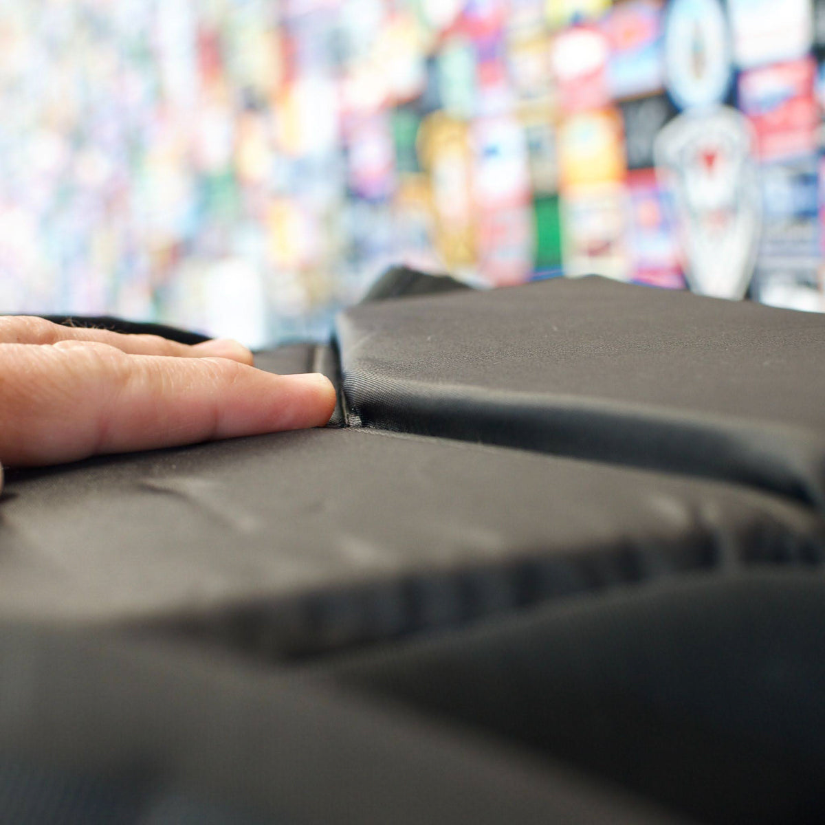 A finger pressing a seam on a black padded fabric with a colorful, blurred background.