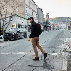 A man wearing a black jacket and Men’s Simple Pants - Midweight ToughDry® crosses an empty small-town street on a cold day.