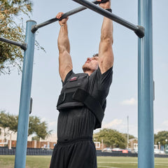 Man in GORUCK weighted vest doing pull-ups outdoors on blue fitness bar