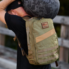 Person carrying a gray camo duffel bag and wearing the olive green Rucker 4.0 outdoors, perfect for adding ruck plates during weighted training pack activities.