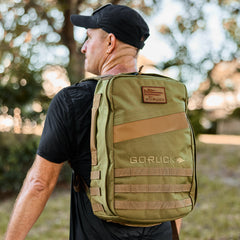 Man outdoors wearing a black cap and shirt, carrying the Rucker 4.0 backpack in green on his back.