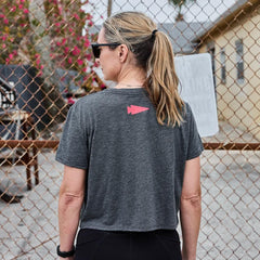 Woman wearing gray GORUCK t-shirt with red logo on back, standing near chain-link fence outdoors