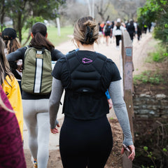 Women walk on a park trail, seen from behind, wearing GORUCK MOTHERUCKER Women's Tee - Tri-BlendX and carrying backpacks.