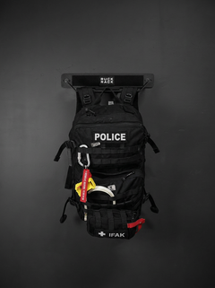 Black tactical police backpack with an IFAK pouch stored on a wall-mounted rack for tactical gear organization.