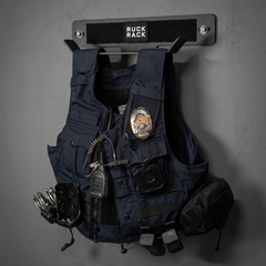 A navy blue police tactical vest with a badge and equipment, hanging on a wall-mounted Ruck Rack for organized tactical gear storage.