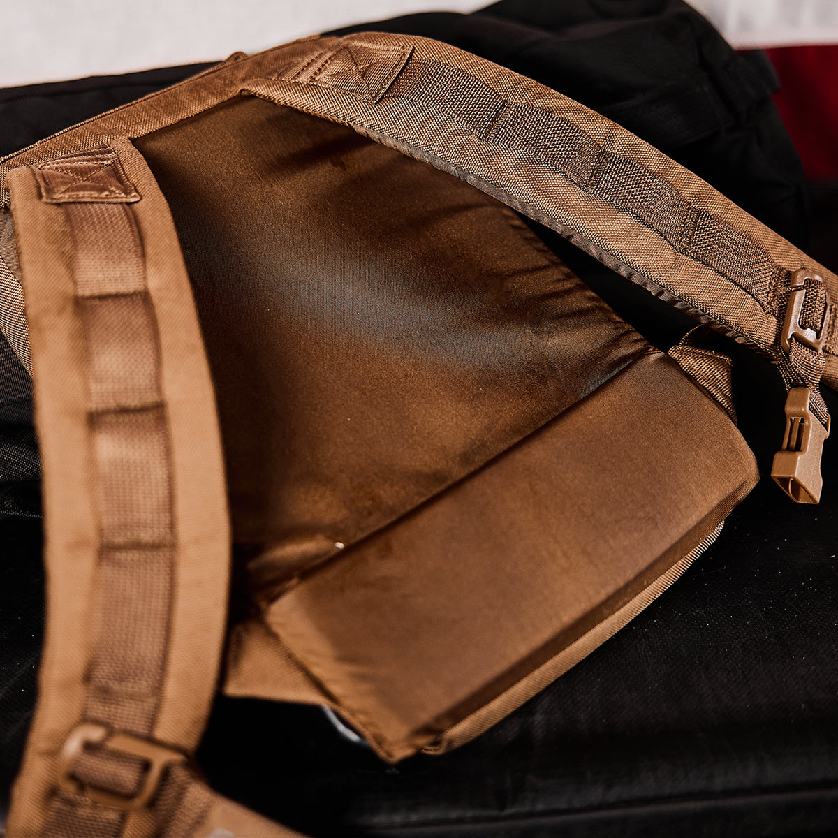 A close-up of brown backpack straps and back padding, resting on a black surface.
