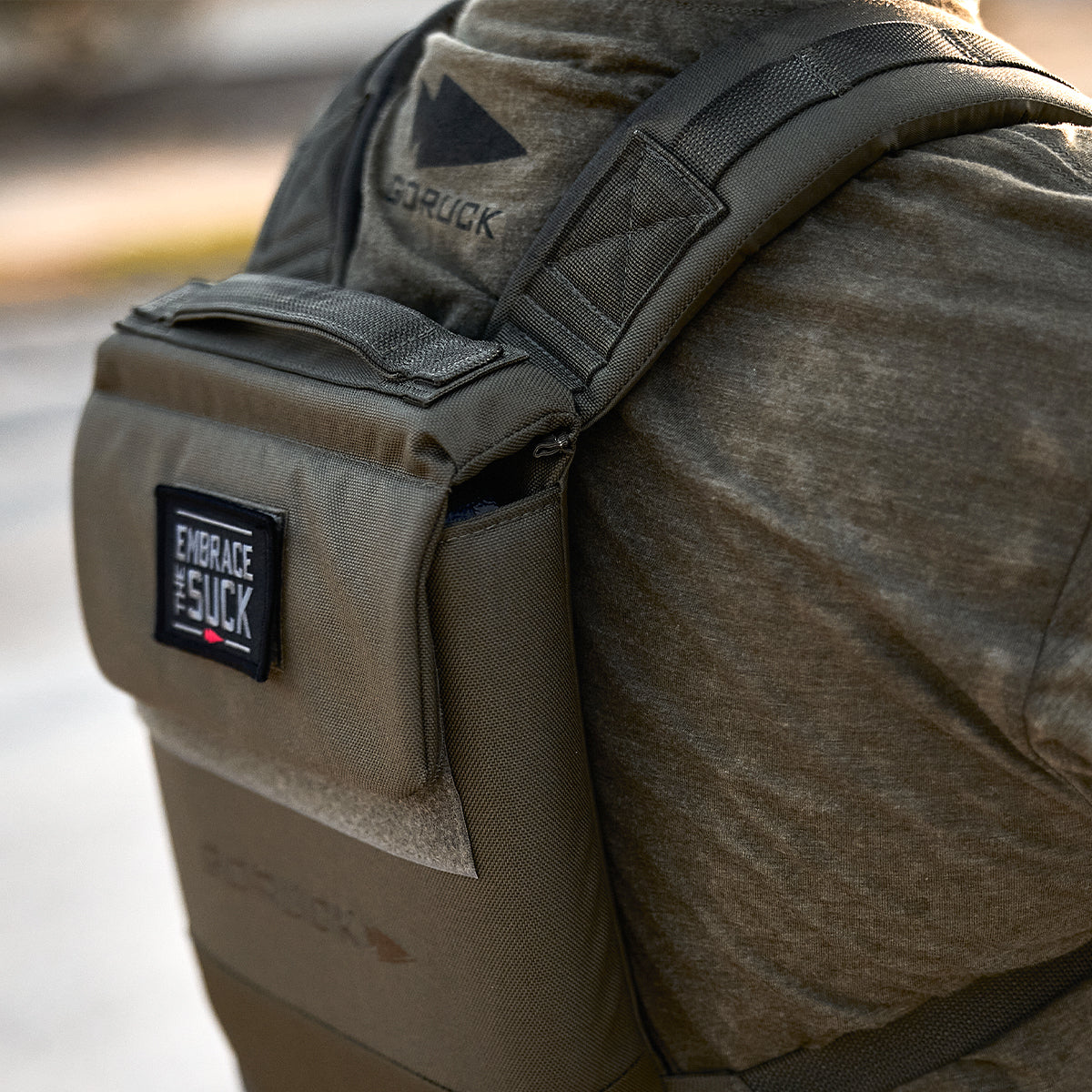 Close-up of a person wearing an olive green tactical backpack with a patch reading 