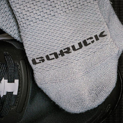 Close-up of gray GORUCK branded performance socks placed on black athletic shoes