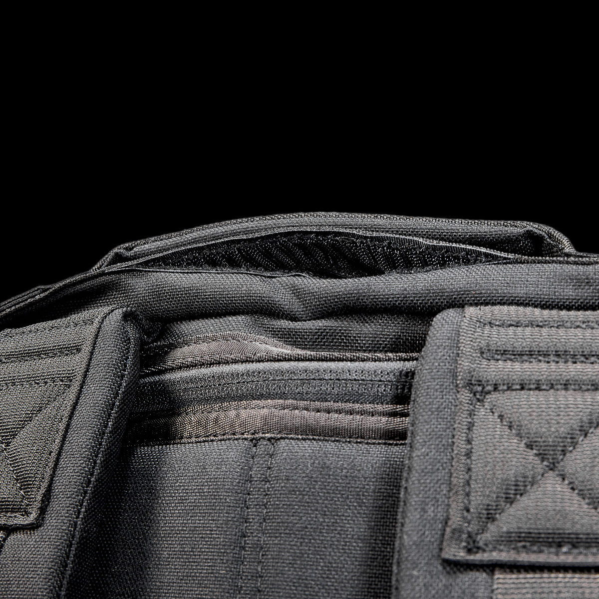 Close-up of the Radio Ruck USA Throwback, a black tactical-inspired backpack with visible stitching and padded shoulder straps, designed for durability and versatility, set against a black background.