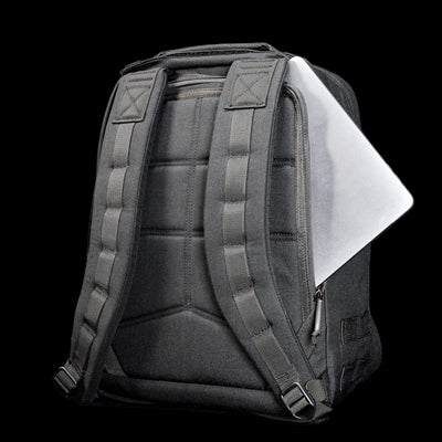 A black Radio Ruck USA Throwback backpack with padded straps, partially unzipped to show a laptop securely stored in its bombproof compartment against a black background.