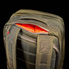 Close-up of an olive green ruck resembling the durable GORUCK GR2 - Cordura model, boasting a vibrant orange interior. It features padded shoulder straps and a partially open top zipper. The ruck appears sturdy with reinforced seams, set against a bold black background, mirroring Special Forces reliability.