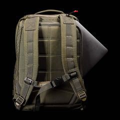 The khaki green GR2 - Cordura backpack by GORUCK, similar to those utilized by Special Forces, features padded straps ideal for rugged outdoor adventures. A laptop can be seen emerging from the top, suggesting ample storage space in this tactical rucksack. The solid black background emphasizes its durable design.