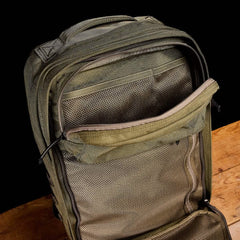 The open GR2 backpack from GORUCK, in green, sits on a wooden surface against a black backdrop. Its Special Forces quality is clear as the unzipped main compartment displays mesh pockets for exceptional organization, making it perfect for those looking for carry-on compliant options.