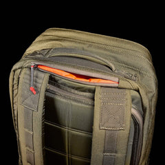 Close-up of the olive green GR2 backpack from GORUCK, showcasing its partially open top zipper that reveals an orange interior. Crafted with Special Forces quality in mind, this backpack boasts sturdy stitching and padded straps for enhanced durability. Set against a black background, its details are highlighted, making it ideal for carry-on compliant travel.