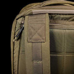 A close-up of the GR2 backpack strap and upper section in olive green against a black background. The strap, featuring detailed stitching and a plastic loop, reflects GORUCK's Special Forces quality. The fabric texture is visible, highlighting its durable material.