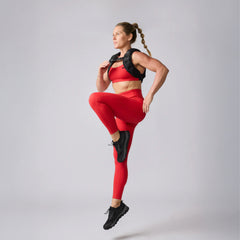 A woman wearing Training Leggings and a weighted vest performs high knees against a plain background.