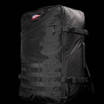 The GR3 - Ripstop ROBIC® by GORUCK is a large black tactical carry-on rucksack made from durable Robic nylon. It boasts multiple straps and buckles, and features a small patch with the American flag and "GORUCK" lettering on the upper part set against a solid black background.