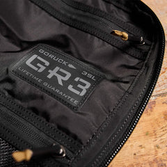 Close-up of GORUCK GR3 35L black rucksack interior with logo patch and zipper on wooden surface