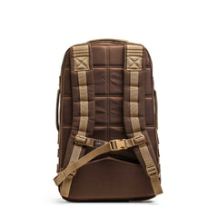 The Rucker 4.0, a brown rucking backpack with padded straps and a chest buckle, is shown from the back against a white background.