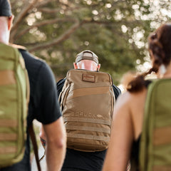 Three people with backpacks walk outdoors; the center person carries a Rucker 4.0 in tan, perfect for fitness and adventure.