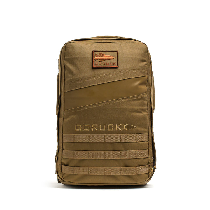 The tan Rucker 4.0 rucking backpack features front zipper pockets, a patch area, and horizontal webbing for attachments—perfect as a fitness rucksack or weighted training bag.