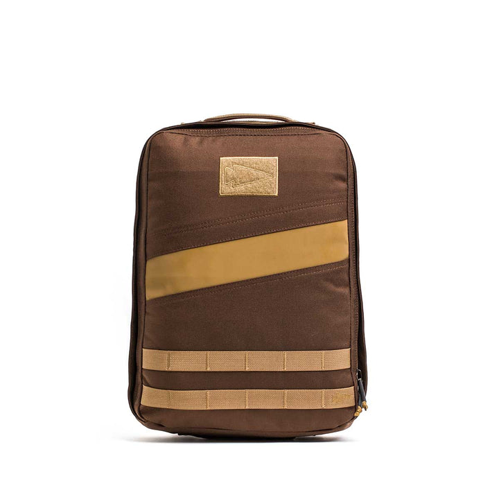 The Rucker 4.0 rucksack, featuring a brown body with tan accents, front handle, and horizontal straps, stands upright against a white background.