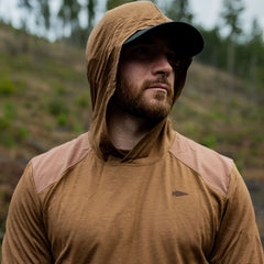 Man outdoors wearing GORUCK brown hooded rucking shirt with arrowhead logo, forest background