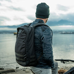 Man wearing GORUCK rucksack by waterfront, outdoor adventure gear, rugged lifestyle scene