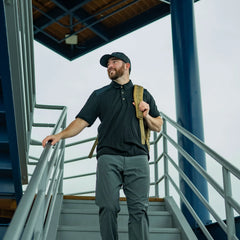 Man wearing GORUCK rucking gear and backpack on outdoor stairs under a metal structure