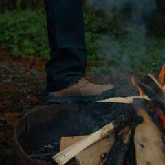 Close-up of rugged brown GORUCK boot stepping near a campfire with burning logs outdoors