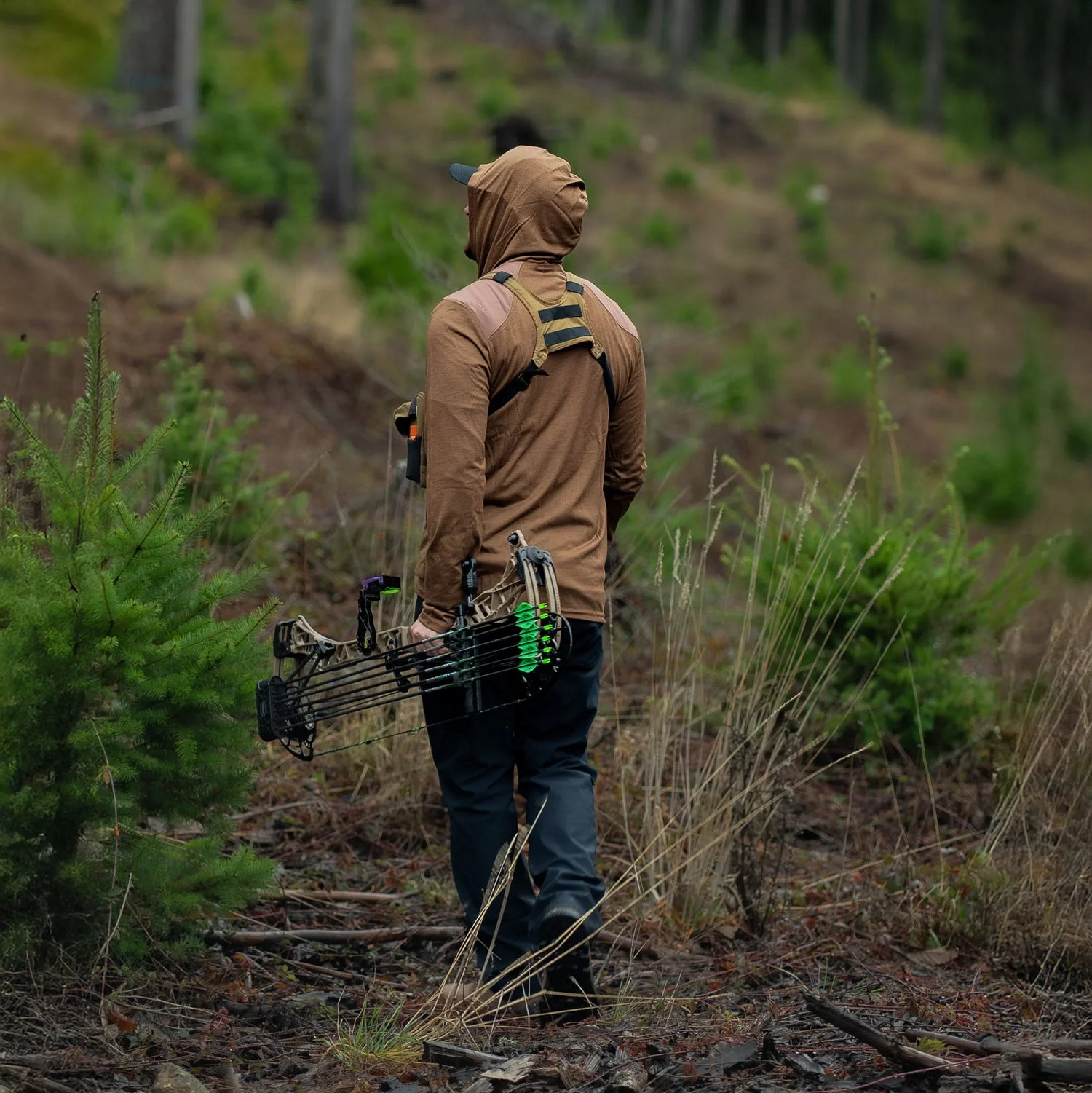 Man rucking in outdoor gear with bow in forest, GORUCK tactical backpack visible