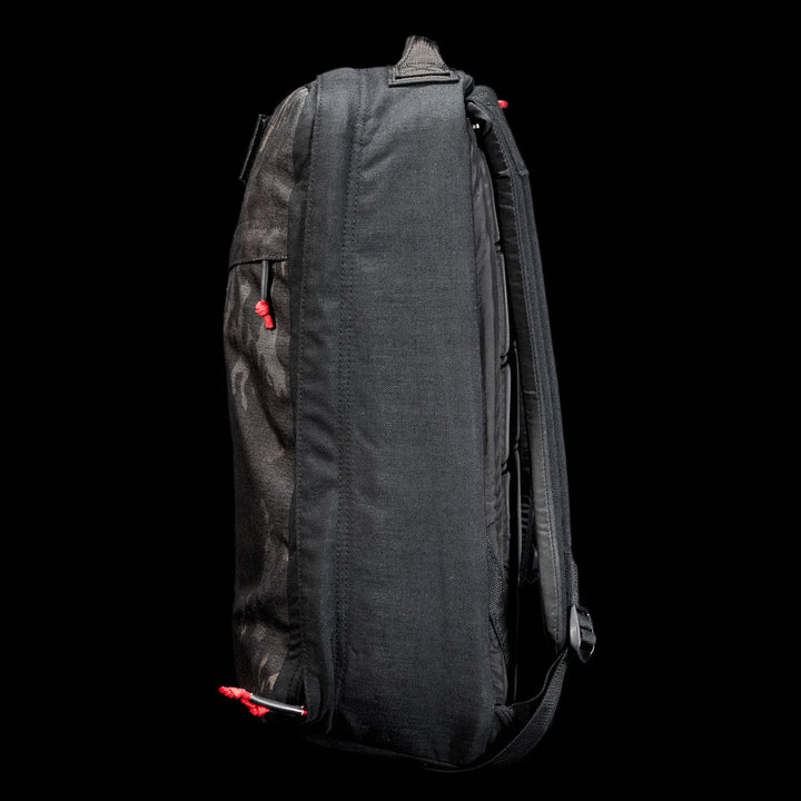 Side view of a black GR1 Shooter 26L - Built by Scars backpack in rugged CORDURA® fabric, with red zipper pulls, shown against a plain black background.