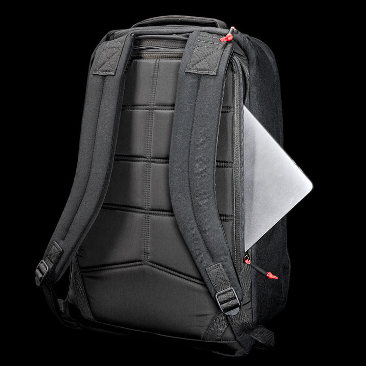 The GR1 Shooter 26L - Built by Scars is a black CORDURA® backpack with padded straps and a laptop partially visible in the side zippered pocket.
