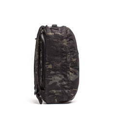 Side view of the GR1 USA Slick - Ballistic Nylon Cordura backpack in black and gray camouflage with shoulder straps, featuring a bombproof laptop compartment, against a white background.