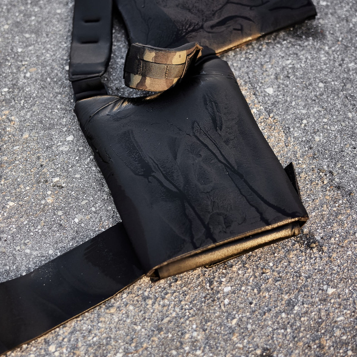 A black weighted vest with a camouflage detail on the strap, resting on asphalt.