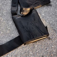 A black weighted vest with a camouflage detail on the strap, resting on asphalt.