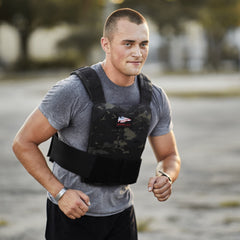 A man in a grey t-shirt and camouflage training weight vest running outdoors.