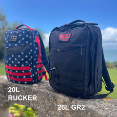 A black GR2 ruck in a carry-on compliant 26L size and a star-spangled 20L pack rest on a stone ledge outdoors, ready for travel adventures.