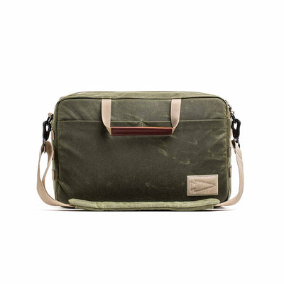 The Shoulder Bag - Waxed Canvas features olive green canvas, beige straps, a front pocket, and a brown-accented handle. Its Martexin Wax finish ensures durability and style—ideal for versatile asymmetrical carries.