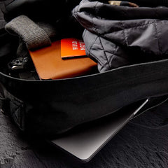 Open black rucking bag with gray jacket, watch, notebook, Field Notes notebook, and laptop inside