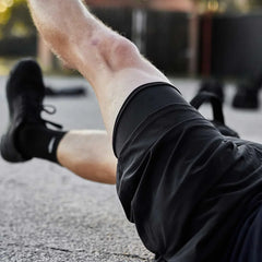 Close-up of a person wearing black compression shorts and black shoes, lying on gravel outdoors