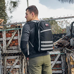 Man wearing black GORUCK Speed grey Robic 16L rucksack standing outside by a chain-link fence