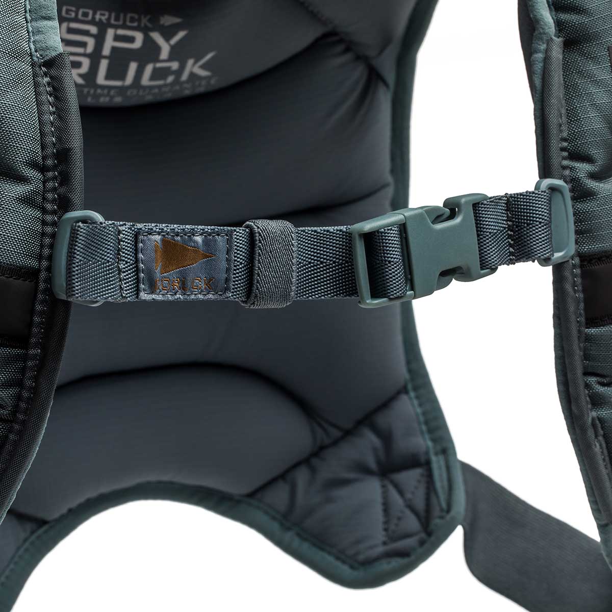 Close-up of a padded Spy Ruck | Women's Weighted Vest strap with a plastic buckle and stitched tag reading 