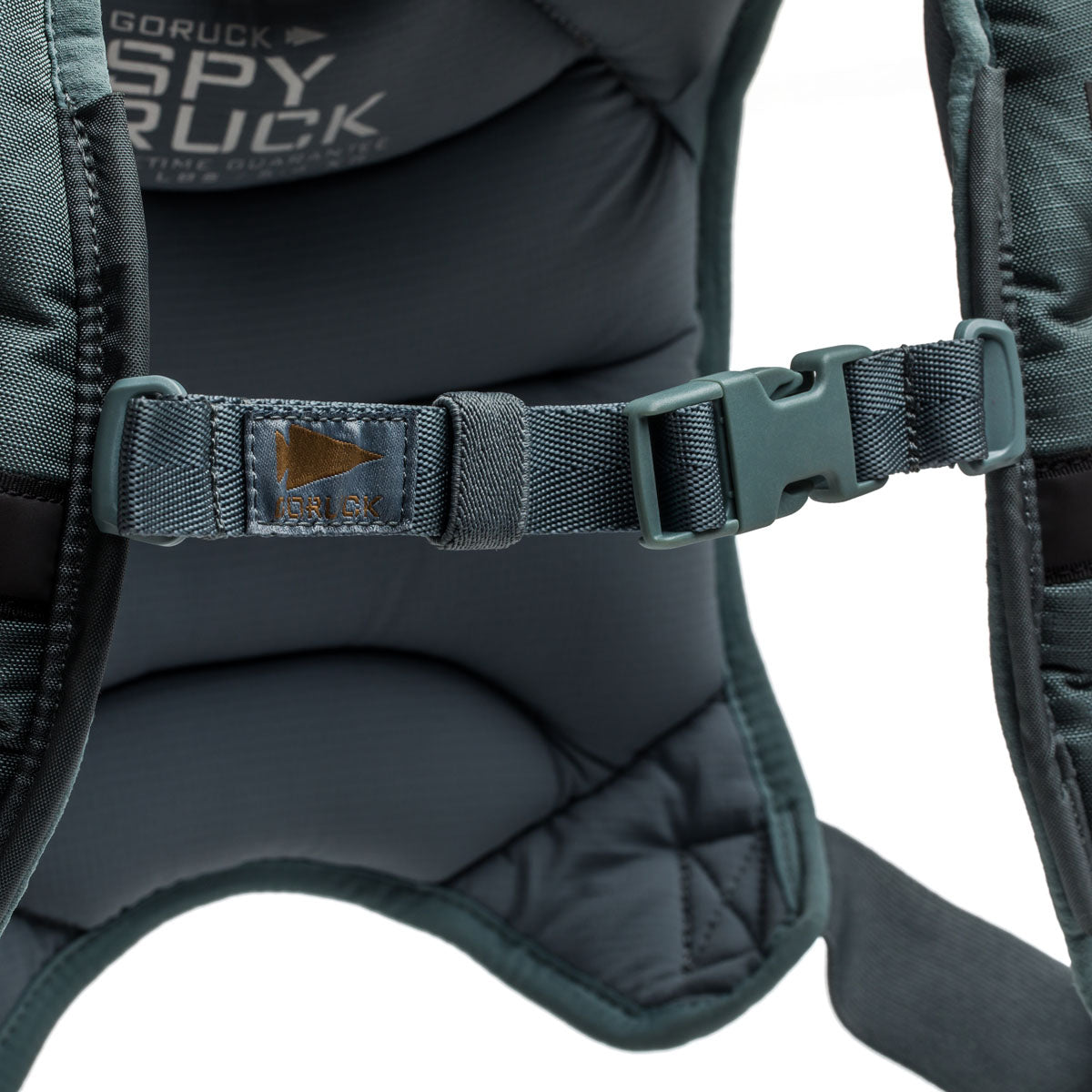 Close-up of a green Spy Ruck backpack strap featuring a plastic buckle and stitched leather 