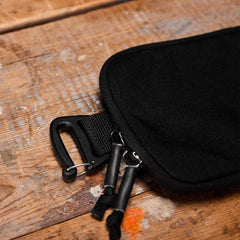 Close-up of black GORUCK sternum pouch with dual zipper pulls on wooden surface