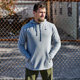 Man wearing GORUCK Subtle Spearhead grey poly-blend hoodie outdoors by chain-link fence