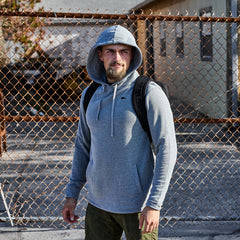 Man wearing grey poly blend hoodie with subtle spearhead logo and black backpack in urban outdoor setting