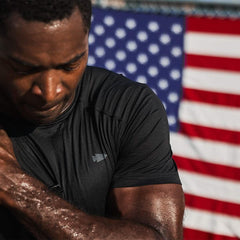 Sweaty man in black workout shirt standing in front of an American flag, focused and determined