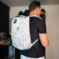 Man wearing GORUCK Arctic camo backpack with American flag patch indoors in casual black shirt