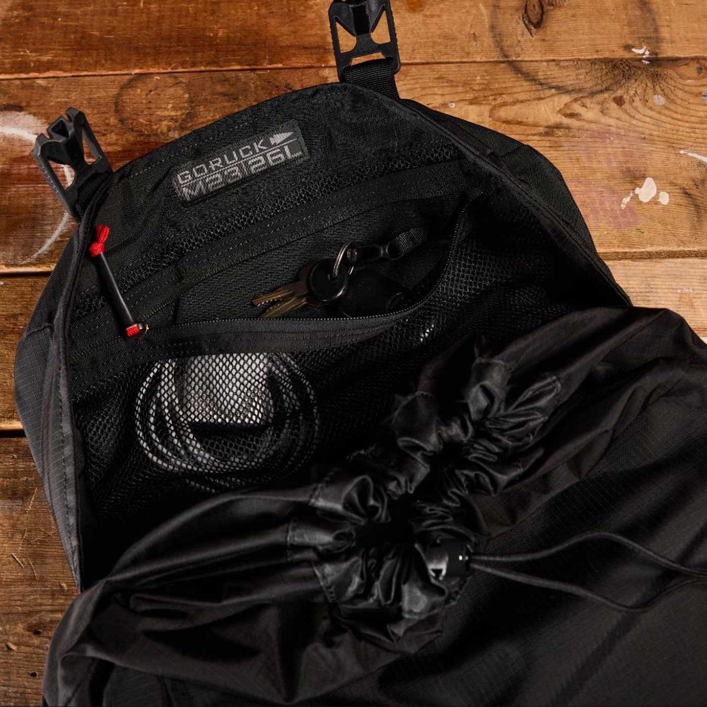Open black backpack with mesh pocket holding keys and cord, on a wooden surface.